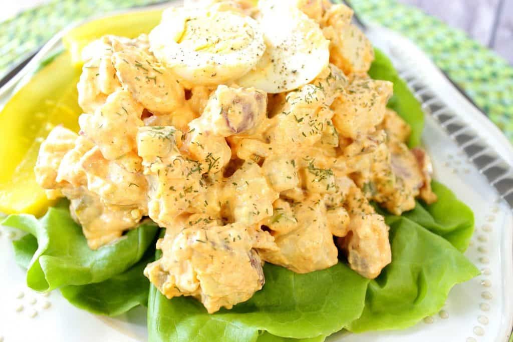 Closeup photo of a plate of potato salad on a white plate on a bed of lettuce.