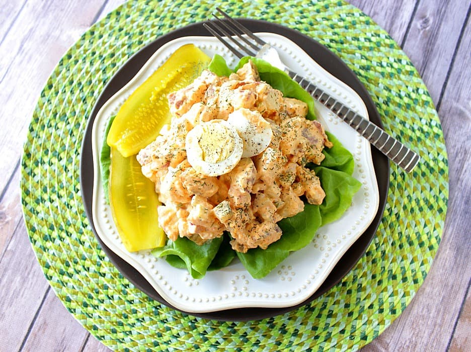 Overhead picture of a plate of potato salad on a green place mat with a fork.