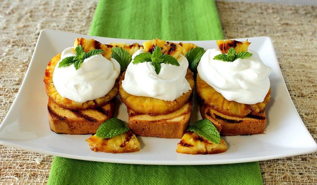 Three slices of grilled pineapple pound cake on a white plate with a green napkin and mint sprigs.