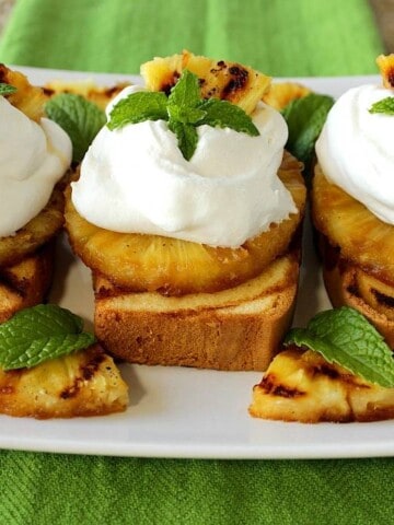 Three slices of grilled pineapple pound cake on a plate with whipped cream and mint.