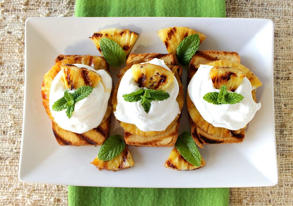Overhead photo of grilled pineapple pound cake slices on a white plate with fresh mint, whipped cream and a green napkin.