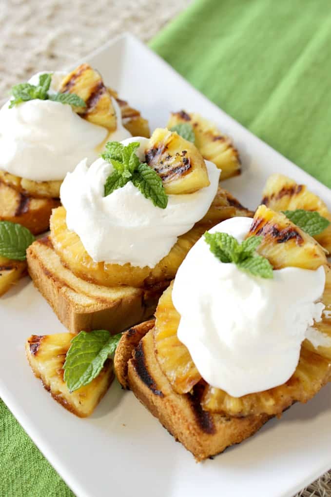 Vertical photo of grilled pound cake with pineapple slices on top along with whipped cream and mint.