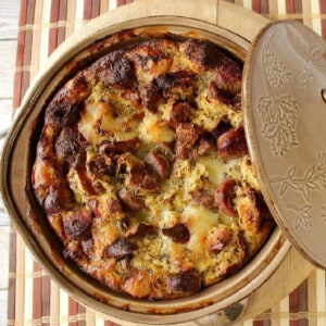 A tan round casserole dish filled with golden brown German Bratwurst Strata.