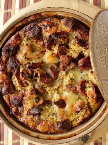 A tan round casserole dish filled with golden brown German Bratwurst Strata.