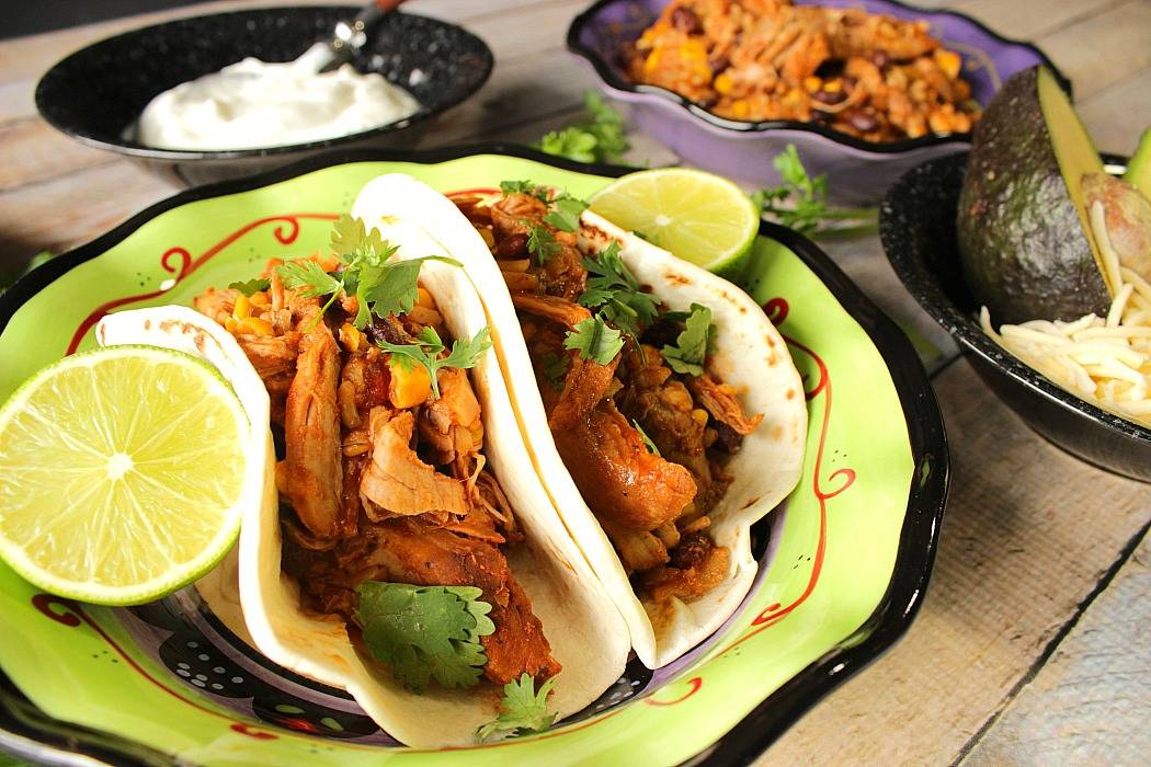 Slow Cooker Shredded Pork Tacos in a green and black bowl with lime wedges and cilantro.