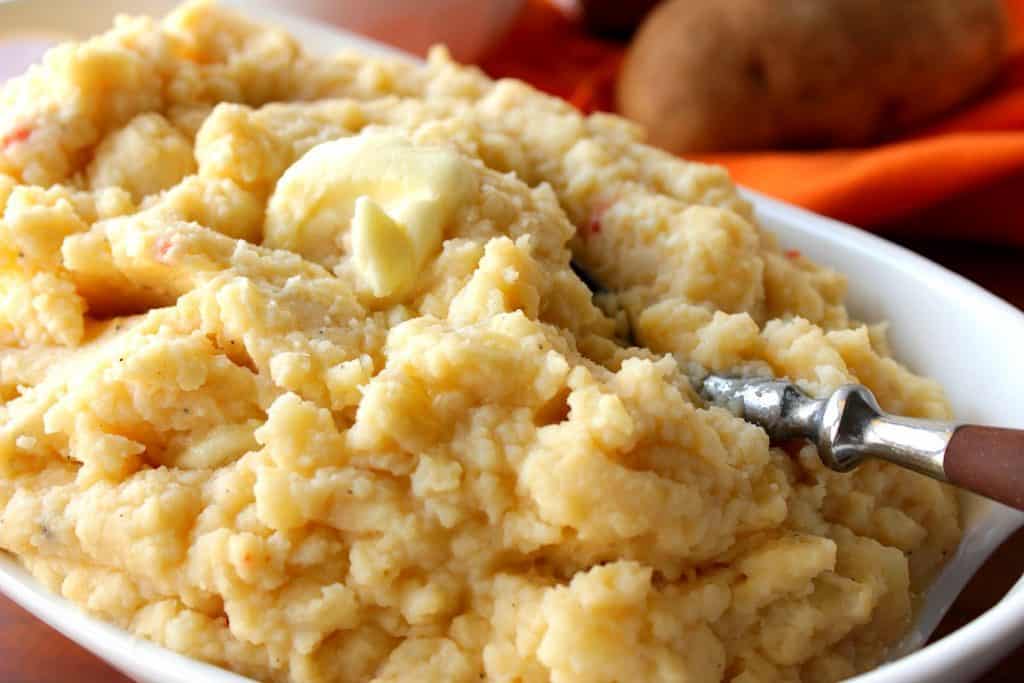 A white bowl filled with Pimento Cheese Mashed Potatoes and a pat of butter.