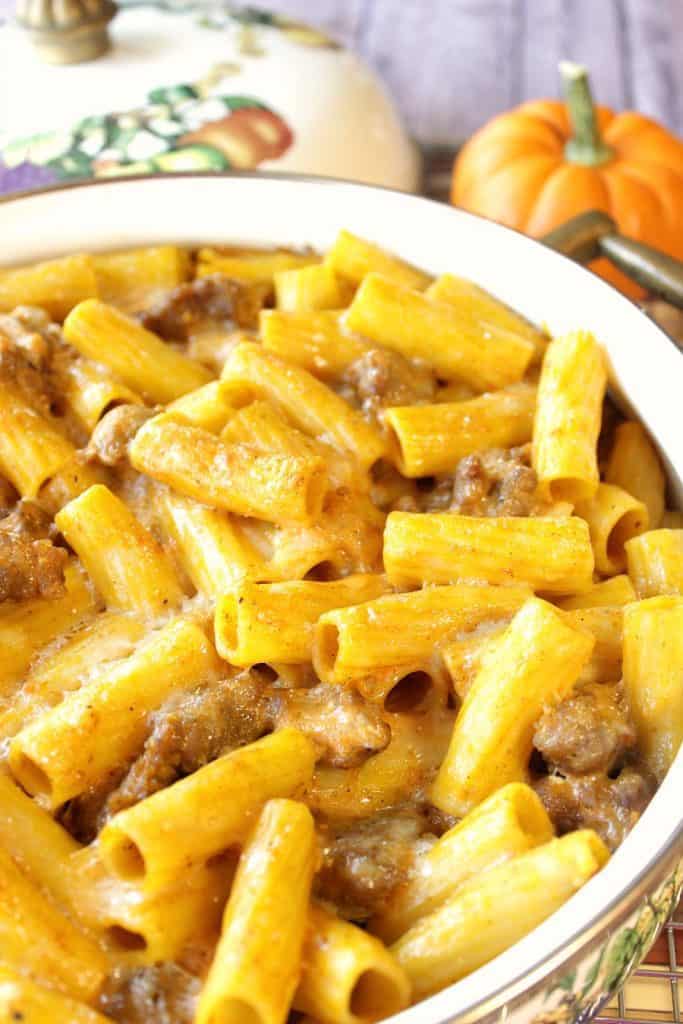 A closeup vertical photo of a casserole dish filled with pumpkin cream pasta with bratwurst