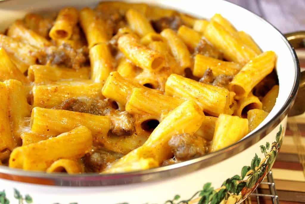 An offset horizontal photo of a casserole dish filled with pumpkin cream pasta with bratwurst