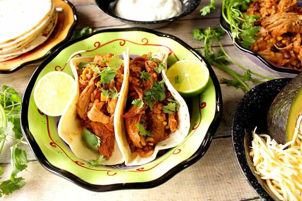 pulled pork tacos on a plate with lime wedges and fresh cilantro