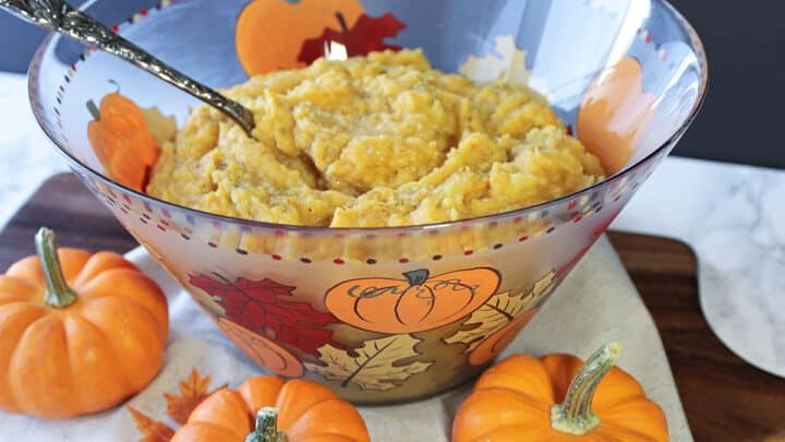 A glass bowl filled with Pumpkin Mashed Potatoes along with baby pumpkins in the foreground.
