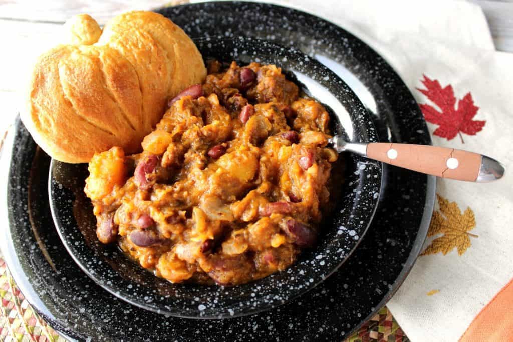 Overhead photo of a black bowl filled with butternut squash chili and a pumpkin shaped biscuit on the bowl.