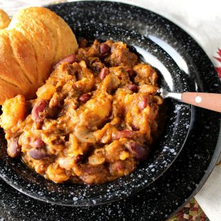 A bowl of butternut squash chili with a pumpkin shaped biscuit.
