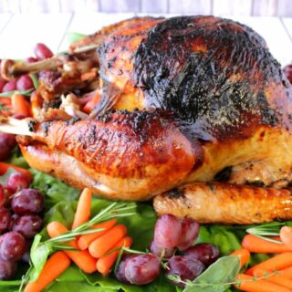 A beautifully browned roasted turkey on a platter with grapes, carrots, and greens.