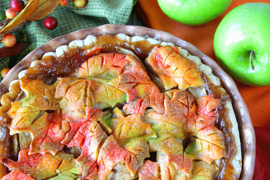 Overhead photo of an autumn leaves apple pie in a pie dish with apples.