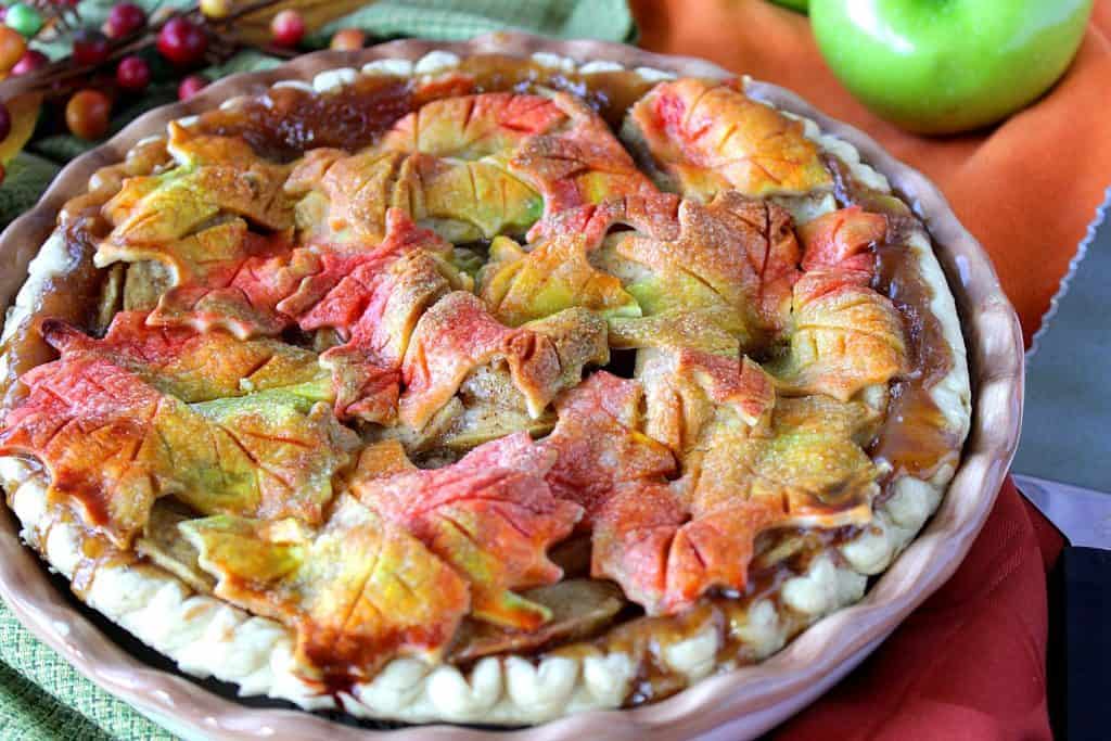A colorful Autumn Leaves Apple Pie with an green apple in the background.