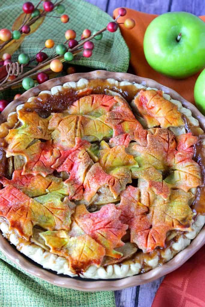 Vertical image of an apple pie with autumn leaves and apples.