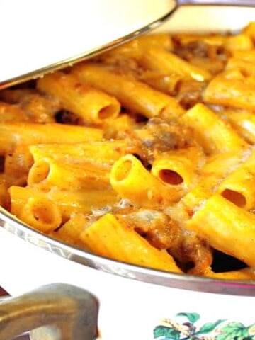 A casserole dish filled with pumpkin cream pasta with bratwurst and a small pumpkin on the side.