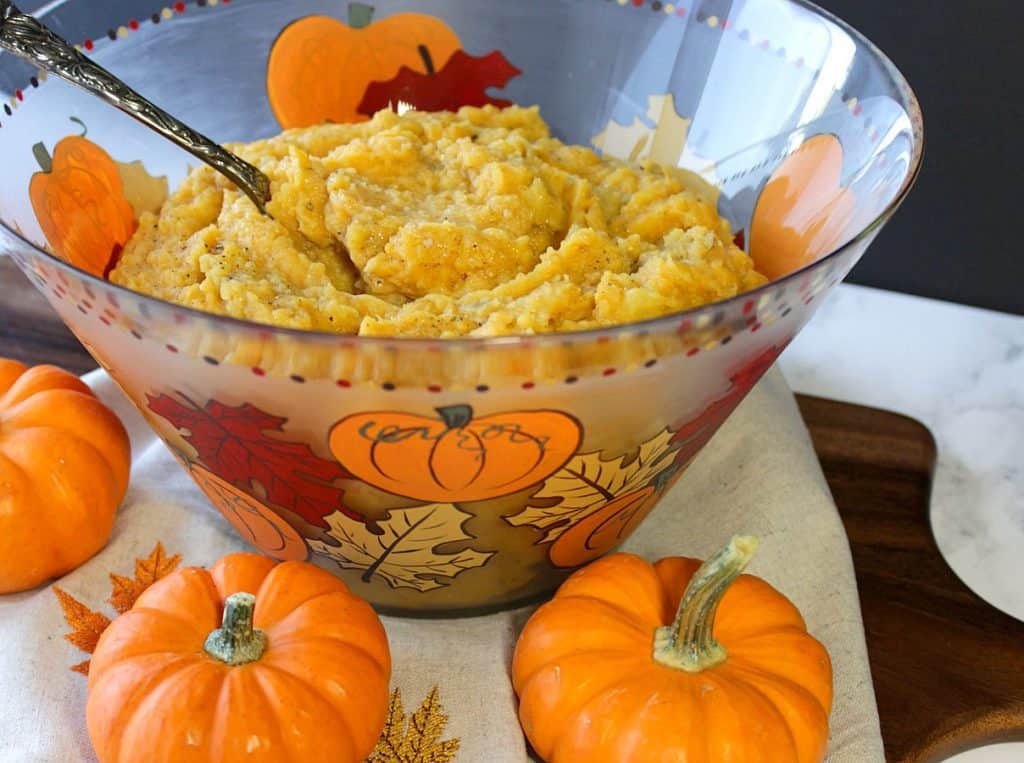 A large glass bowl of pumpkin mashed potatoes with mini pumpkins and leaves painted around the bowl.