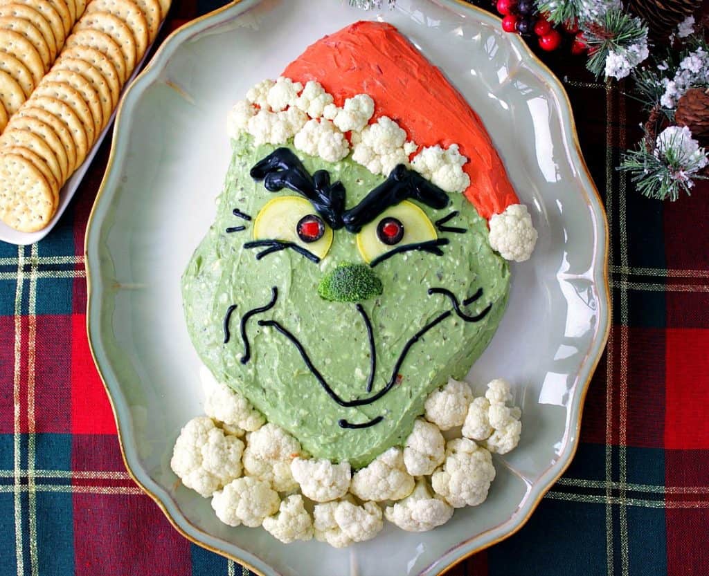 Overhead photo of a grinch guacamole on a plate with cauliflower fur and crackers.