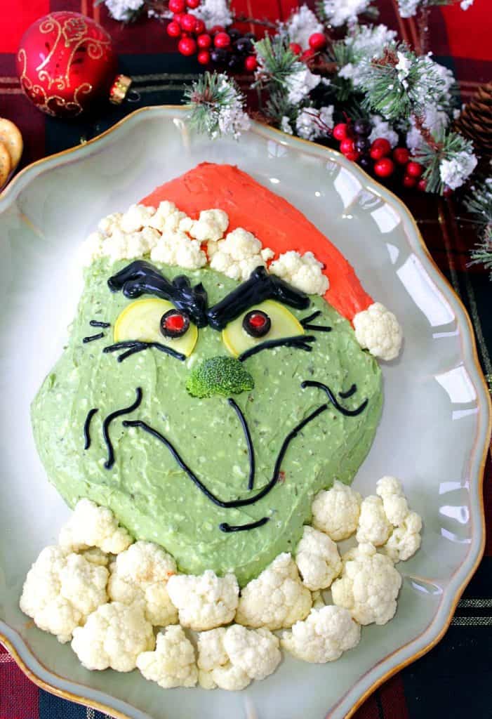 Vertical overhead photo of Grinch guacamole on an oval platter with cauliflower fur and a broccoli nose.