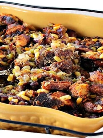 A mustard yellow casserole dish filled with Pretzel Roll Stuffing along with a serving spoon.