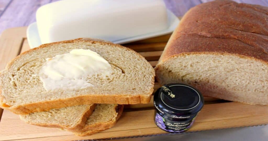 An overhead photo of a loaf of Whole Wheat Honey Ricotta Bread with a small jar of jam, and some smeared butter on the bread.