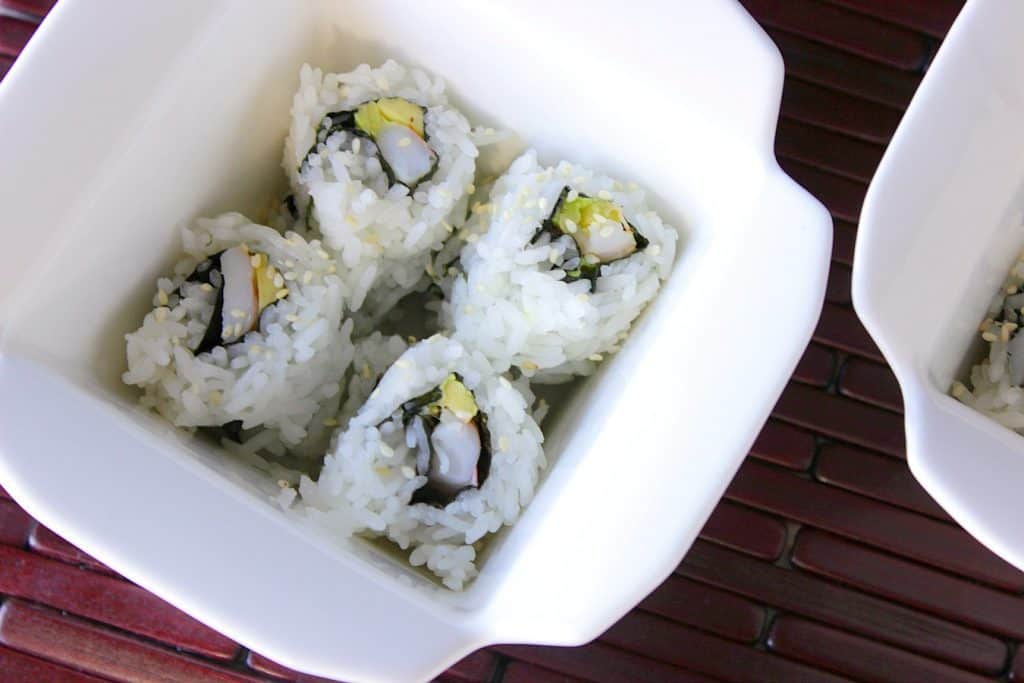 Closeup of Homemade Avocado Shrimp Sushi Rolls in a takeout container.