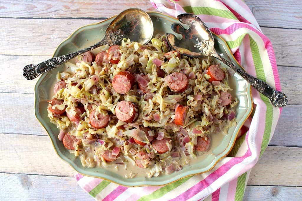 Overhead photo of a platter of creamed cabbage with caraway and sausage along with serving spoons.