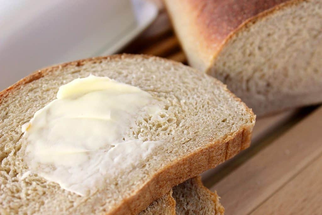 A stack of homemade Whole Wheat Honey Ricotta bread in the foreground and a loaf in the backgroung.