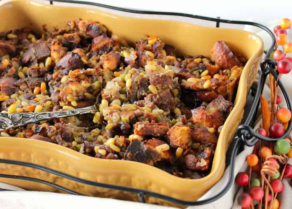 A horizontal photo of buttery Pretzel Roll Stuffing in a yellow baking dish with a serving spoon