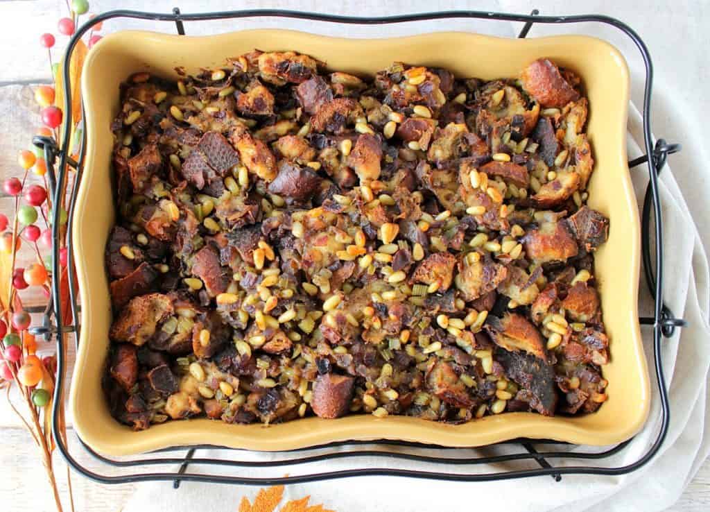 Overhead photo of a yellow casserole dish filled with pretzel roll stuffing and pine nuts.