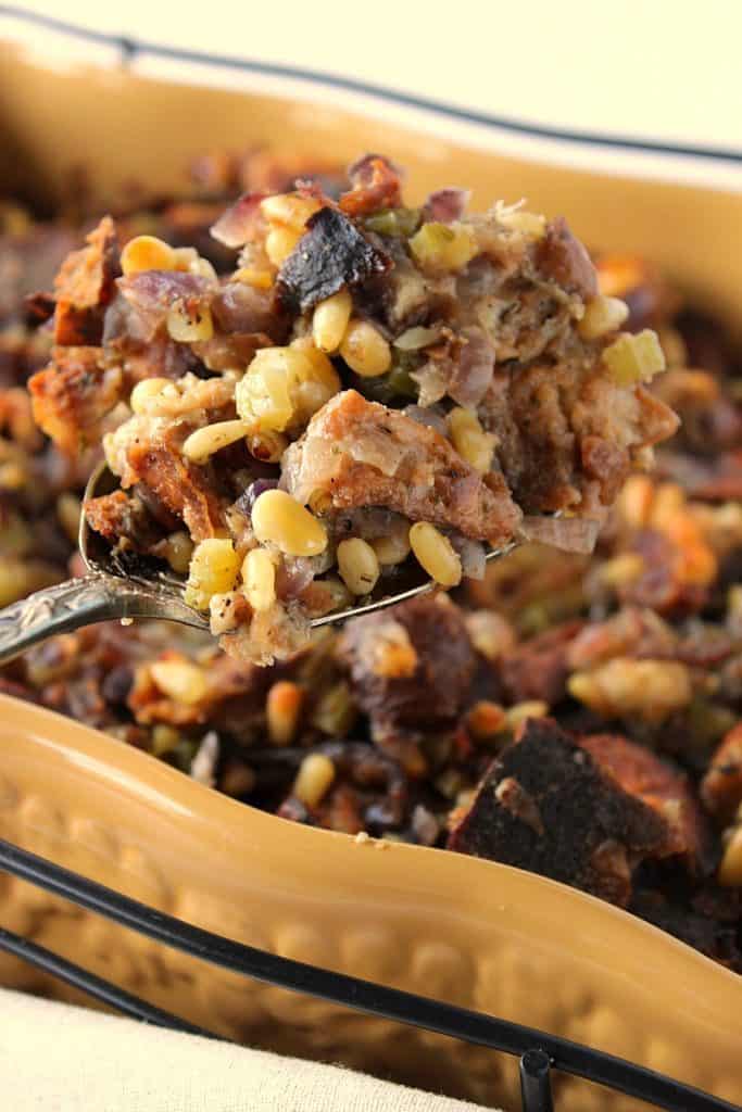 A closeup photo of Pretzel Roll Stuffing Recipe on a serving spoon with pine nuts and onions