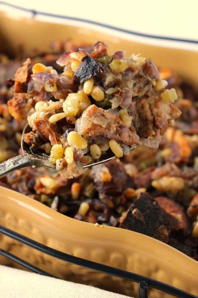 A closeup photo of Pretzel Roll Stuffing Recipe on a serving spoon with pine nuts and onions