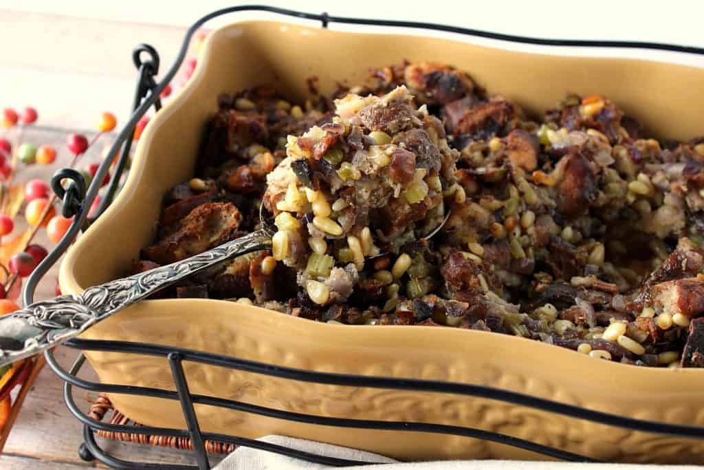 A horizontal photo of Pretzel Roll Stuffing with Pine Nuts in a baking dish with a serving spoon.
