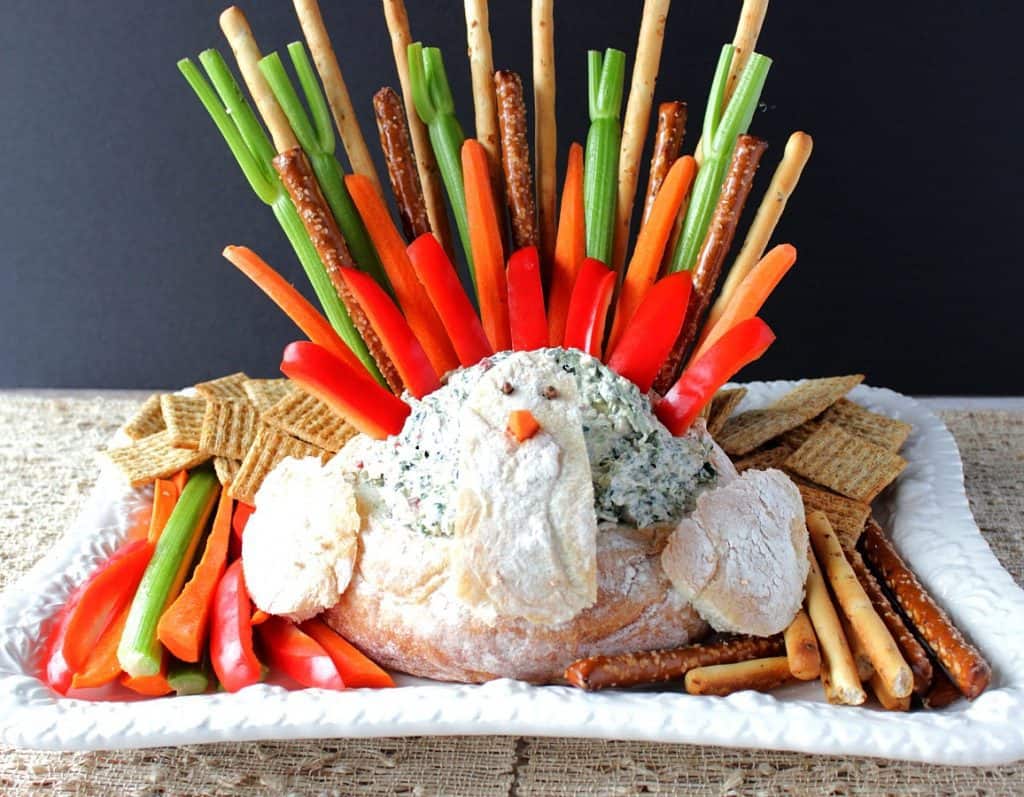 Horizontal photo of a turkey bread bowl appetizer with spinach ranch dip and colorful dippers as tail feathers.