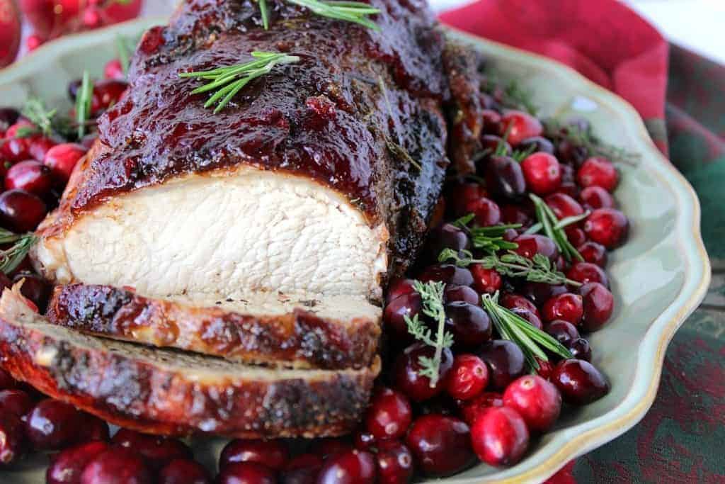 Sliced Pork Roast with Cranberry Relish Glaze on a platter with fresh herbs and cranberries.