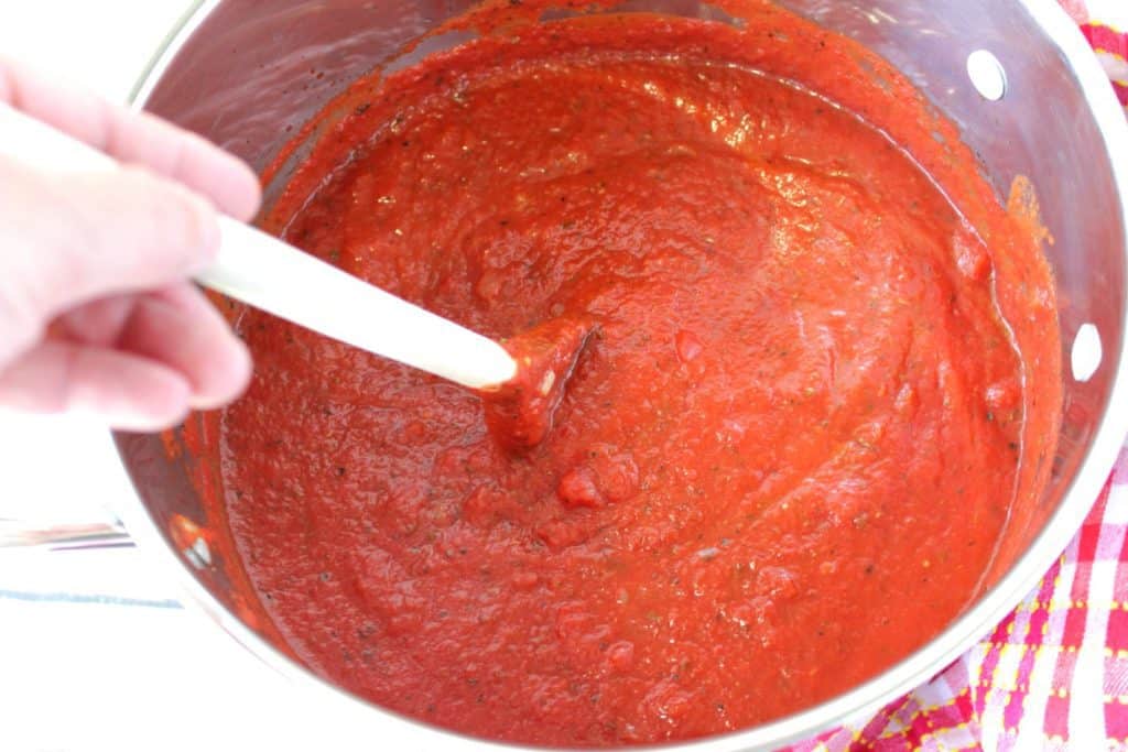 Overhead photo of a hand with a wooden spoon stirring a stockpot filled with classic marinara.
