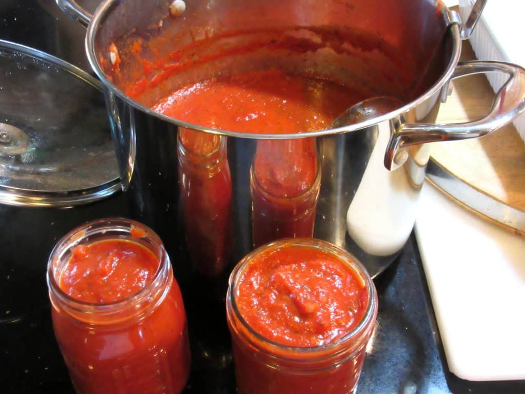 A stockpot filled with classic marinara sauce with two filled glass jars in the foreground.