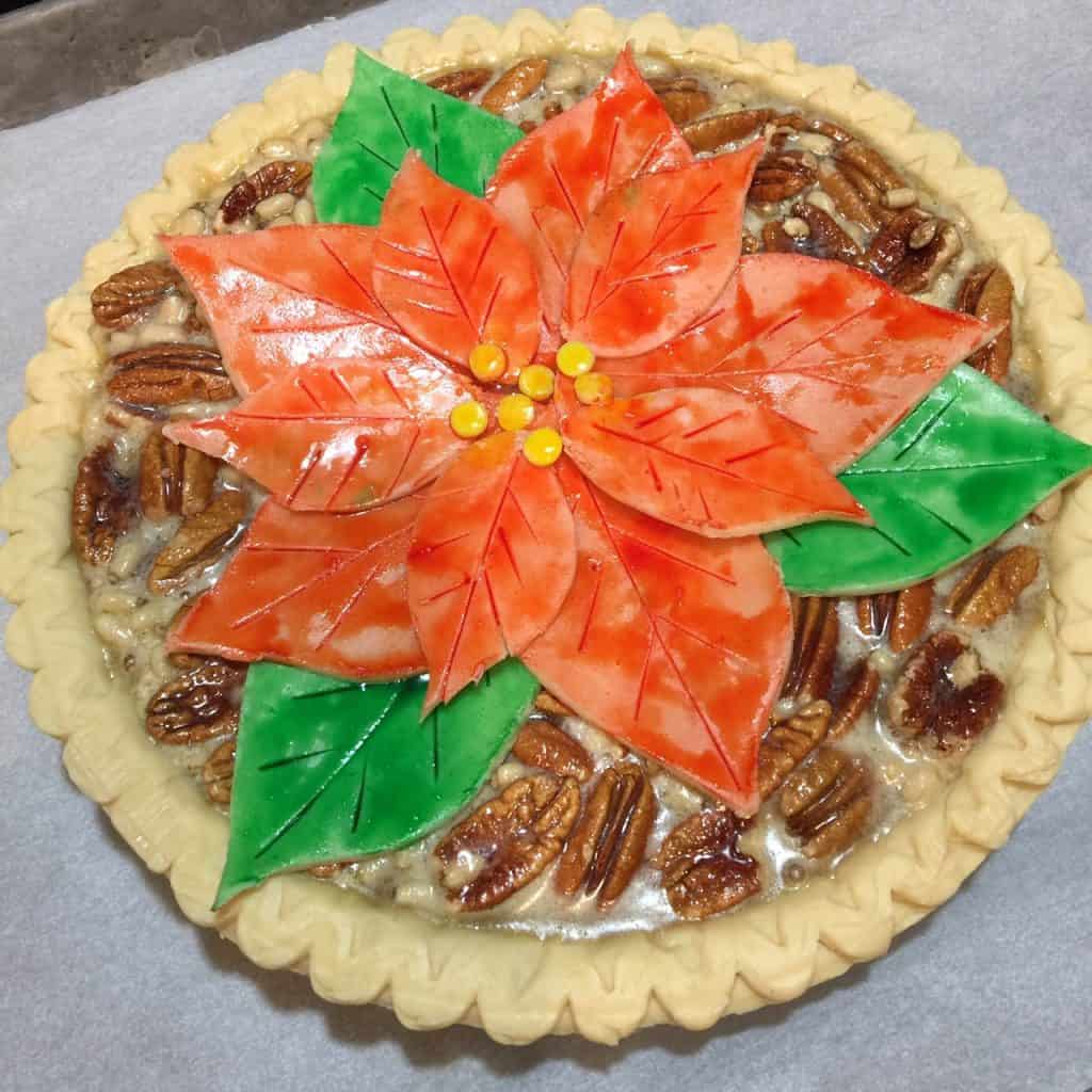 A square photo of an unbaked painted poinsettia pie with red and green leaves.