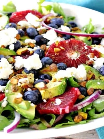 An offset horizontal photo of a Blood Orange Salad in a white bowl with blueberries, avocados, pistachios and feta cheese.