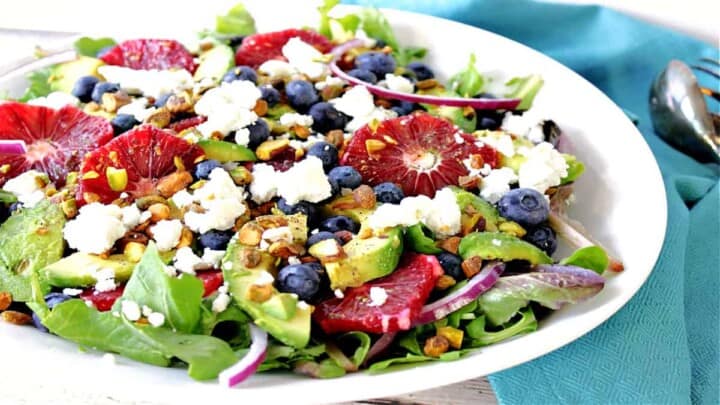 An offset horizontal photo of a Blood Orange Salad in a white bowl with blueberries, avocados, pistachios and feta cheese.