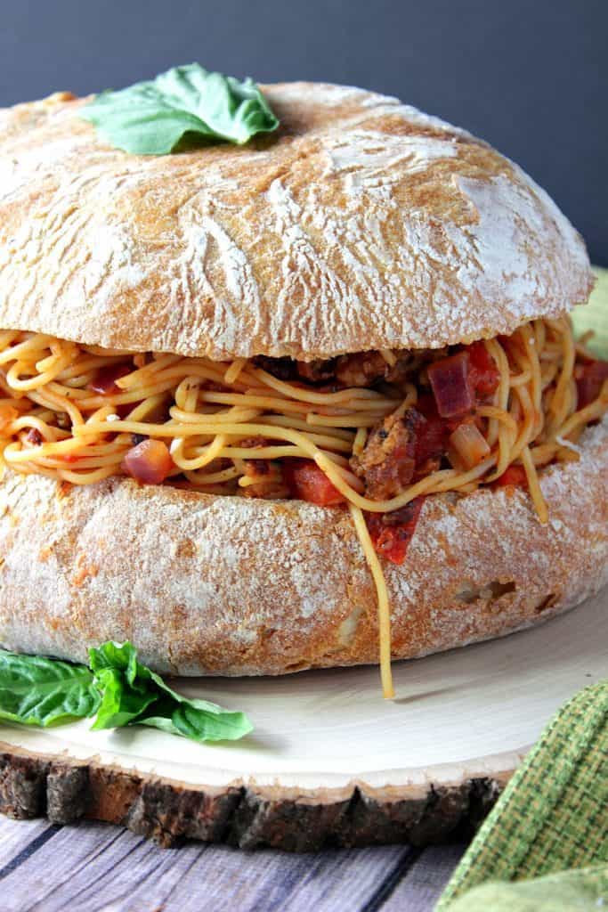 Closeup photo of spaghetti stuffed garlic bread with a fresh basil leave on top.