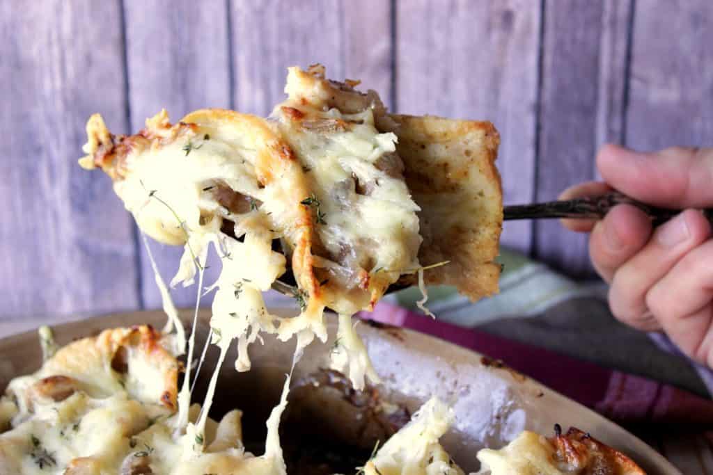 A hand holding a spoon with a serving of Caramelized Onion Stuffed Shells.