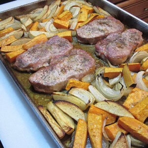 Four boneless pork chops on a sheet pan with apples, onions, and sweet potatoes.