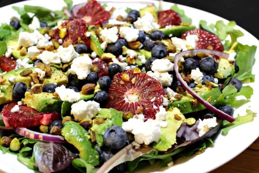 Salad on a white plate featuring blood oranges, blueberries, and feta cheese