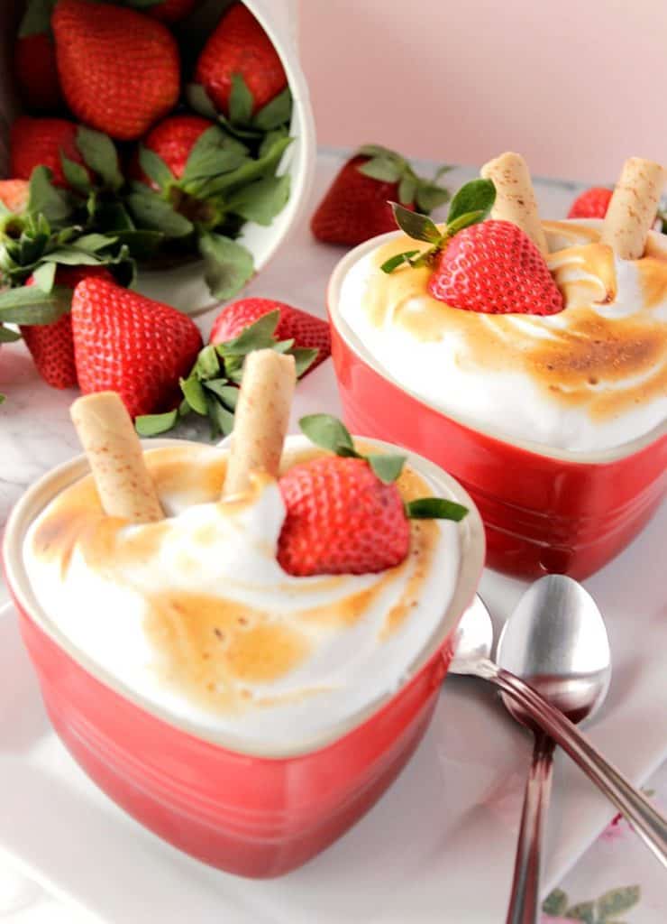 Baked Alaska for Two. Baked Alaska for Two on a white plate with a fallen bucket of strawberries in the background..
