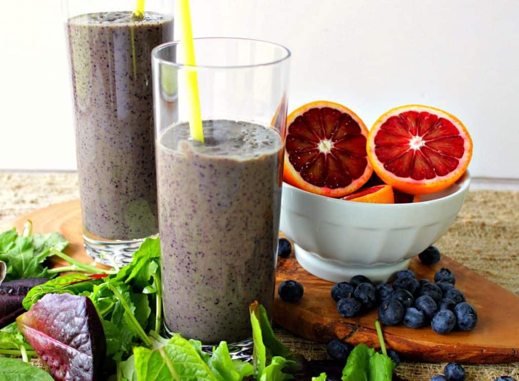 Two glasses of blood orange smoothies with assorted lettuces on a wooden board.