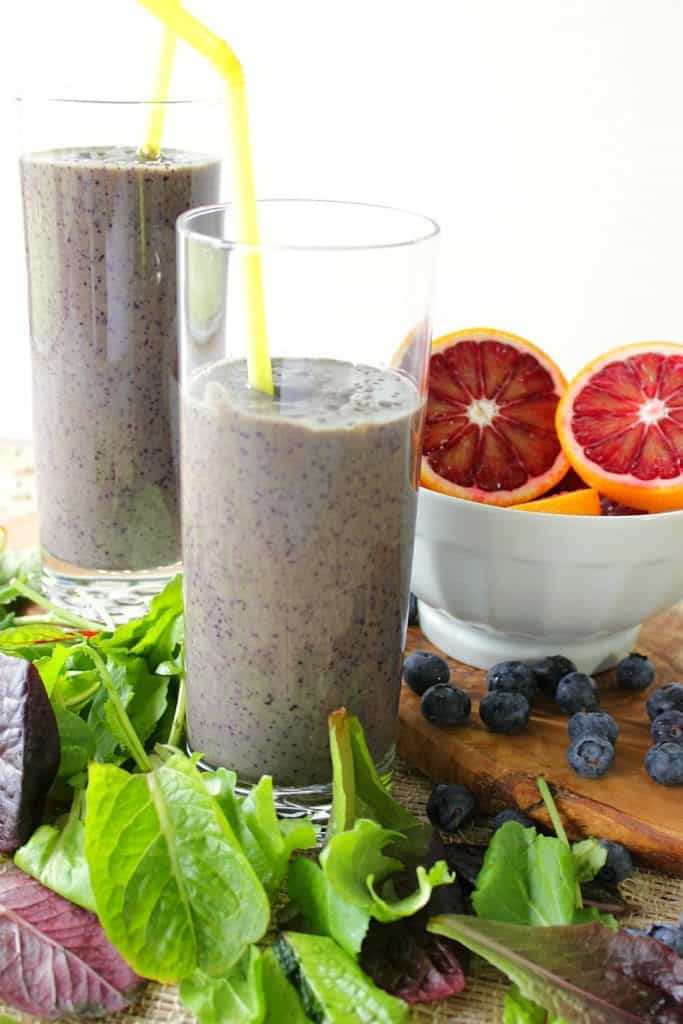 2 blood orange blueberry breakfast smoothies with straws and a bowl of cut oranges