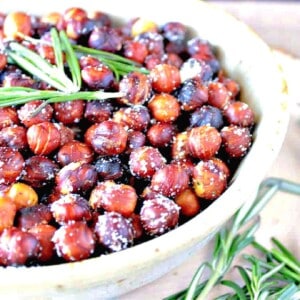 Skillet Roasted Rosemary Hazelnuts in a white bowl with fresh rosemary.