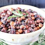 A white bowl filled with Roasted Rosemary Hazelnuts with fresh rosemary for garnish